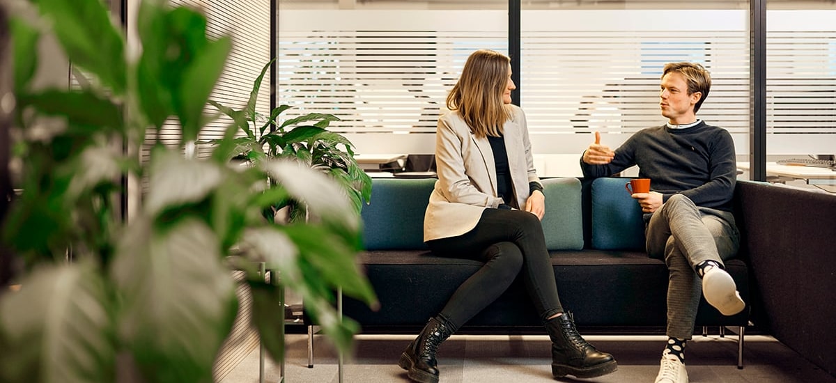 To ansatte i BN Bank sitter i en sofa med en kaffekopp og snakker, til illustrasjon for bedriftskunde i BN Bank