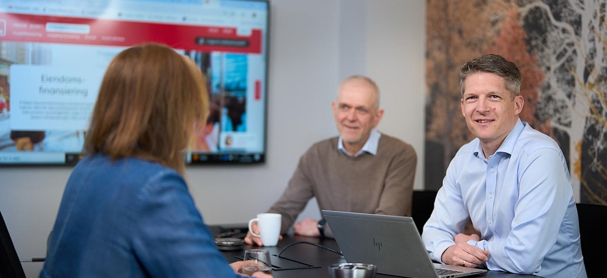 3 ansatte på møterom med pc, til illustrasjon for eiendomsfinansiering