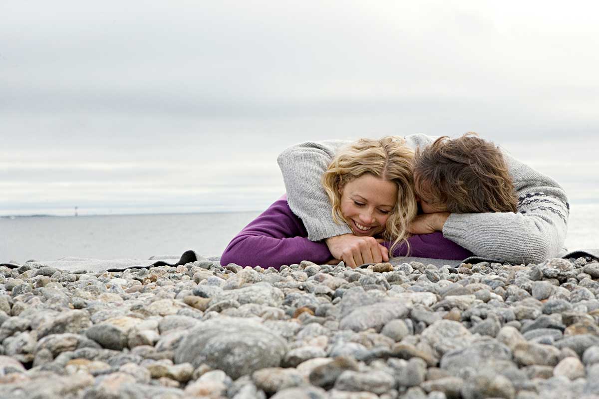 Par ligger på stranda og ler, til illustrasjon for å kjøpe seg inn i bolig