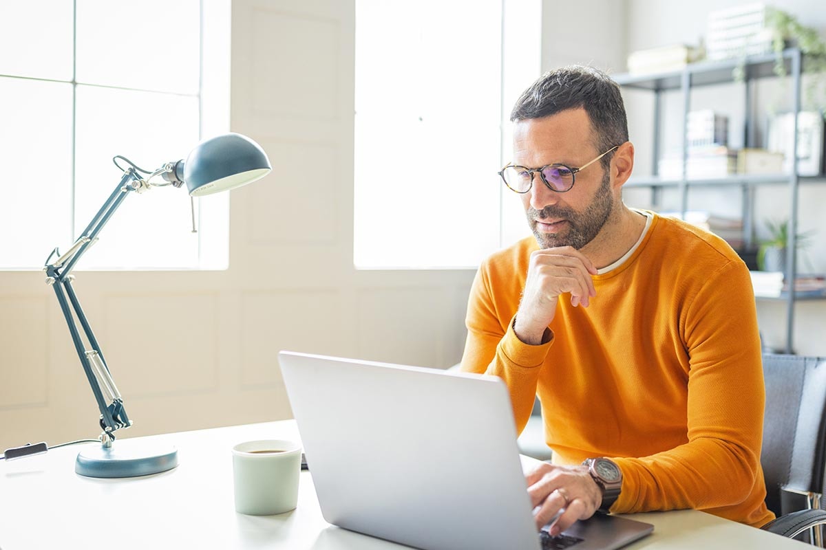 Mann med oransje genser og briller jobber på en laptop, til illustrasjon for betalingsanmerkning