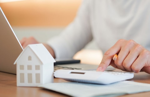 Dame sitter ved bord og skriver på kalkulator, til illustrasjon for refinansiere forbruksgjeld