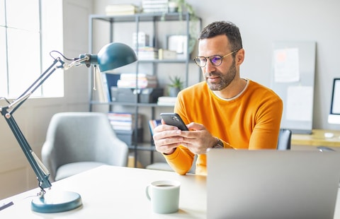 Mann med laptop ser på mobilen sin, illustrasjon til pensjonssparing