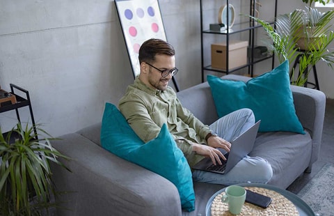 Mann sitter i sofa og jobber på PC, til illustrasjon for hvordan spare penger