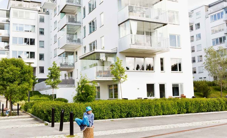Gutt med bøttehatt sitter på en stokk fremfor en boligblokk, til illustrasjon for sekundærbolig