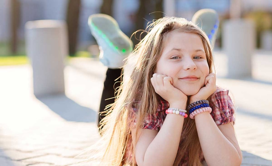 Jente ligger ute på brosteiner og smiler, til illustrasjon for barnekort