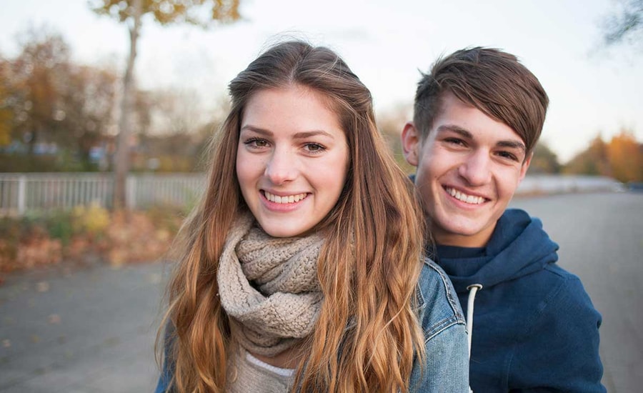 Ung jente og gutt smiler, med løv i bakgrunnen, til illustrasjon for endelig myndig