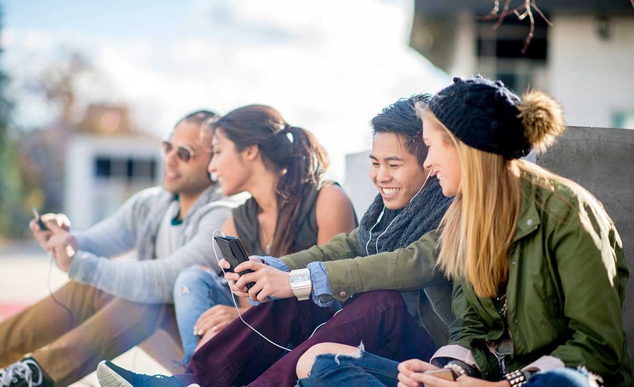 Ungdommer sitter på bakken og ser på mobilene sammen, til illustrasjon for bank for barn og ungdom