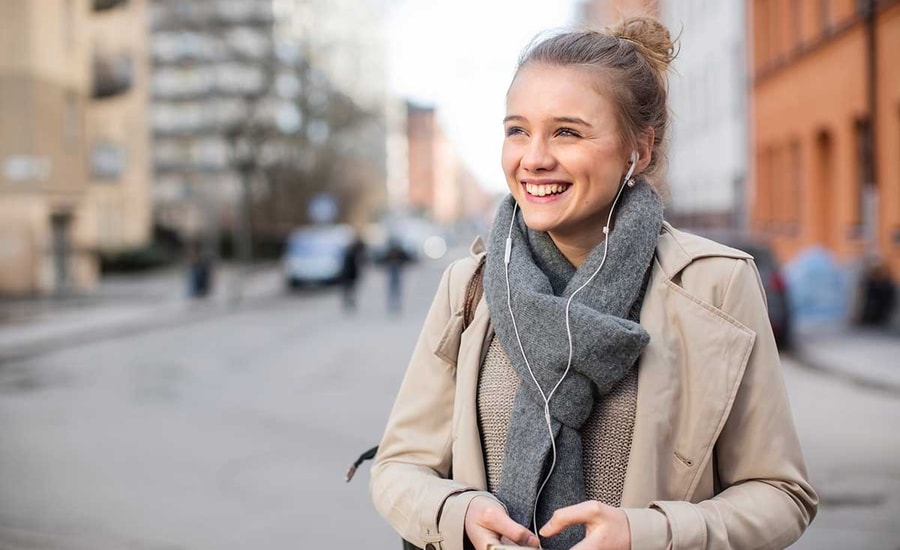 Ung jente hører på musikk ute, til illustrasjon for ungdomskort