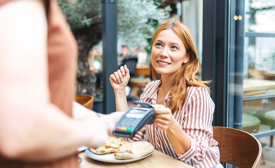 Dame på cafe tapper kort på terminal, til illustrasjon for bankkort
