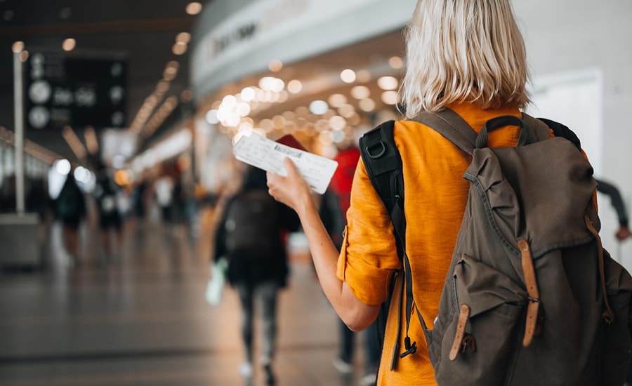 Dame med sekk og holder en flybillett i hånda på en flyplass, til illustrasjon for kredittkort