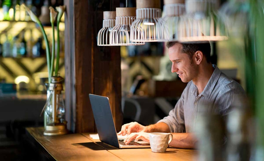 Mann sitter på cafe og ser på laptop, til illustrasjon for mobil-og nettbank