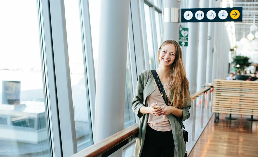 Jente står på flyplassen med mobilen i hånda, til illustrasjon for mobilbank