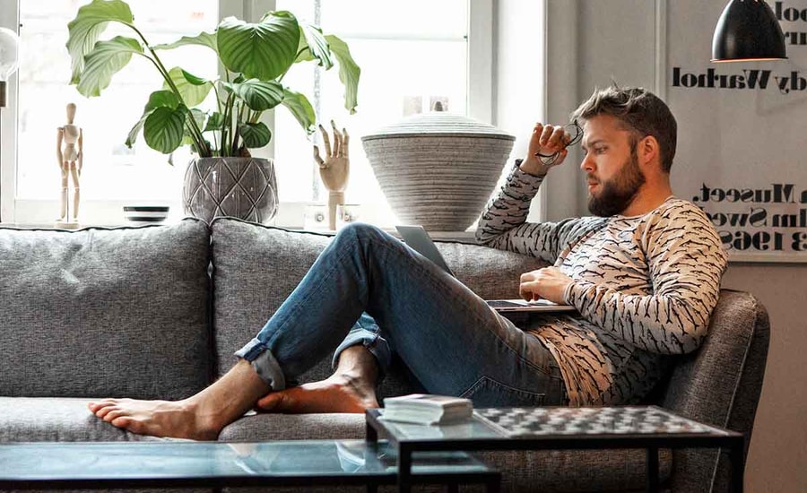 Mann sitter på sofaen og ser på laptop, til illustrasjon for nettbank