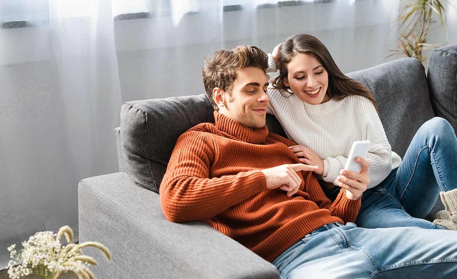 Par ligger i sofaen og smiler mens de ser på mobilen, til illustrasjon for felleskonto