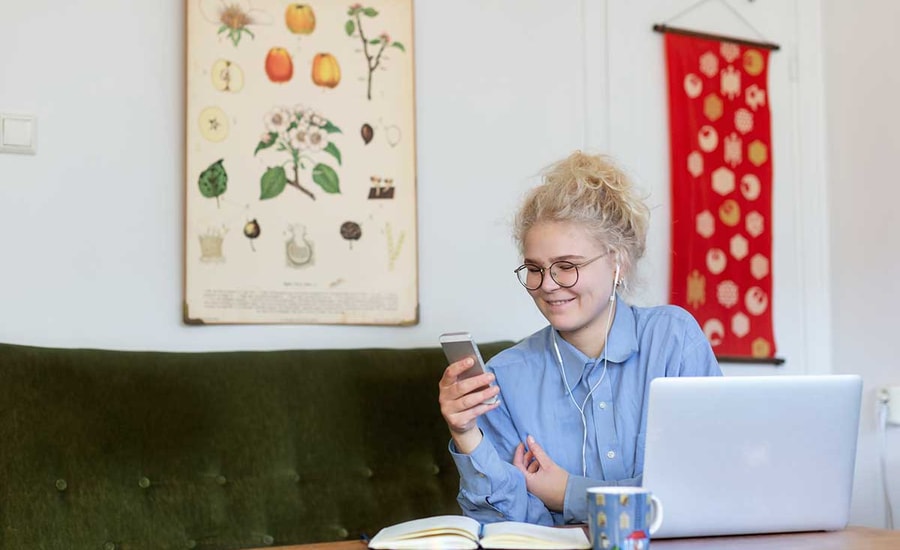 Jente sitter i grønn sofa og ser på mobilen med hodetelefoner, til illustrasjon for husleiekontrakt