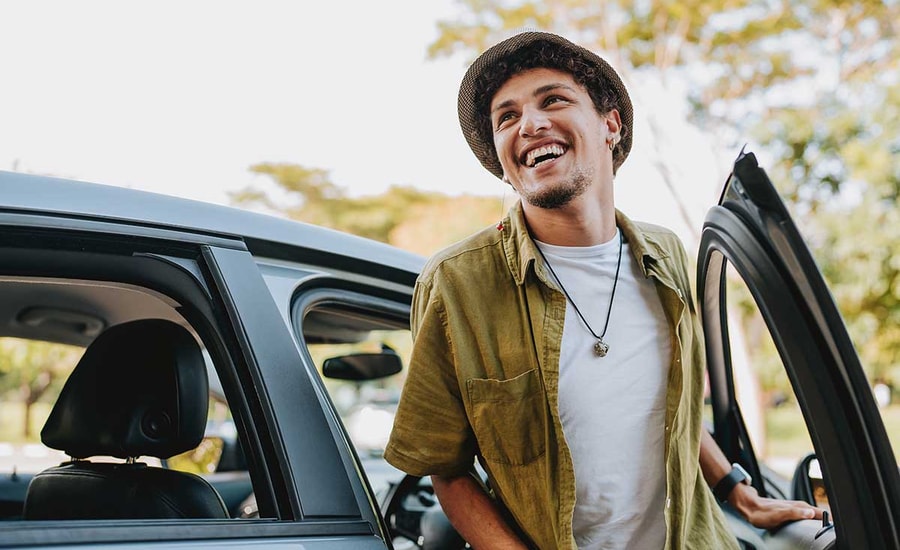 Mann smiler mens han går ut fra en bil, til illustrasjon for billån