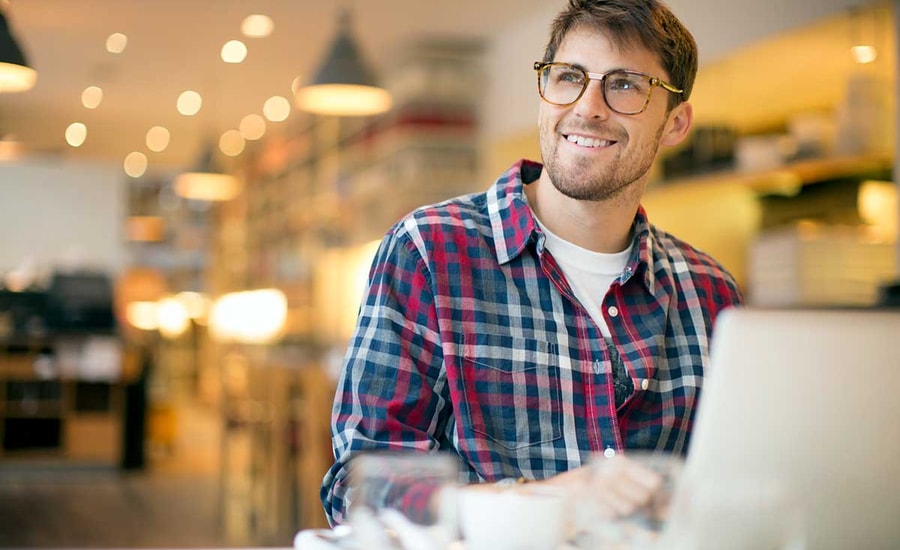 Mann med briller smiler ved pc, til illustrasjon for avdragsfrihet på boliglån