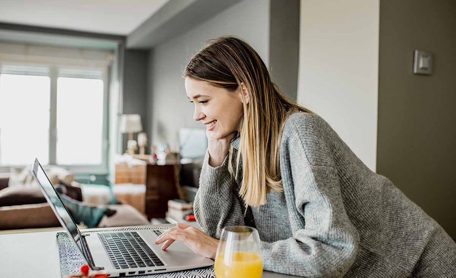 Ung kvinne lener seg over kjøkkenbenken og jobber på en PC, til illustrasjon for bytte bolig