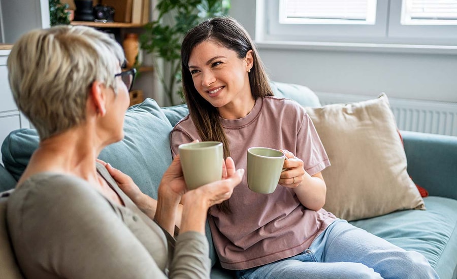 To kvinner sitter i en sofa og drikker kaffe, i forbindelse med hvordan hjelpe barna inn på boligmarkedet