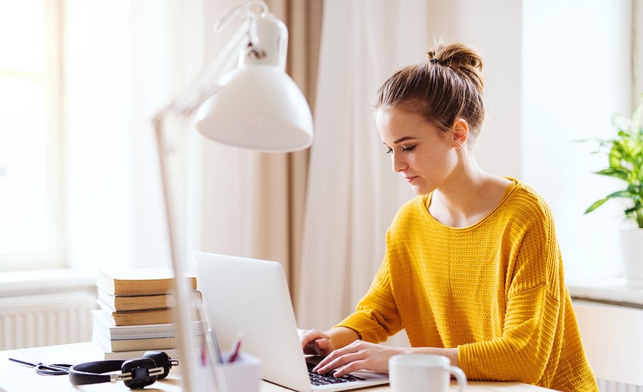 Jente i orange genser med PC, til illustrasjon for ung voksen på vei inn i voksenlivet