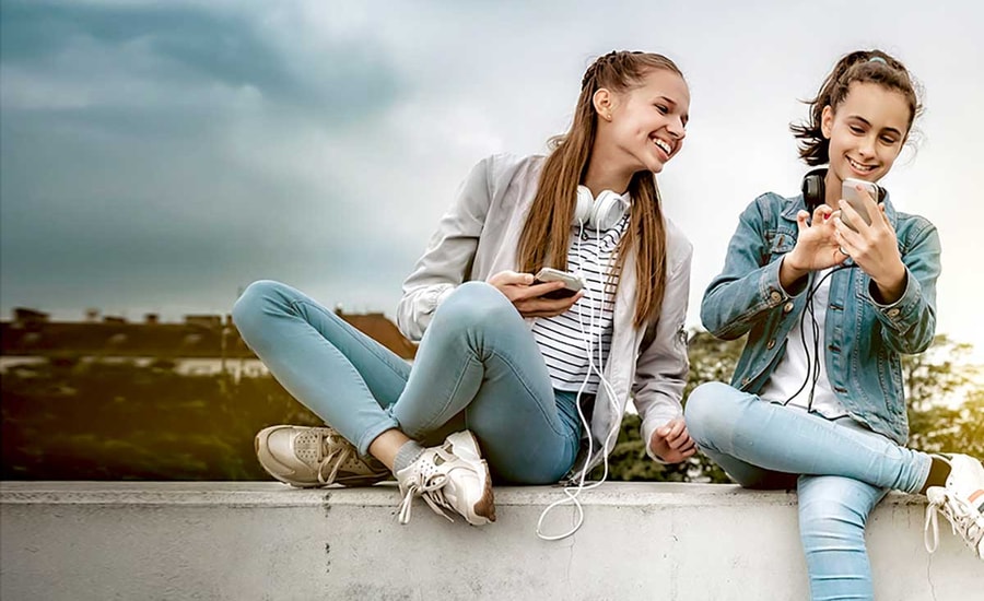 To tenåringstjenster med headset rundt halsen og mobilen i handa, til illustrasjon for sparekonto barn og ungdom
