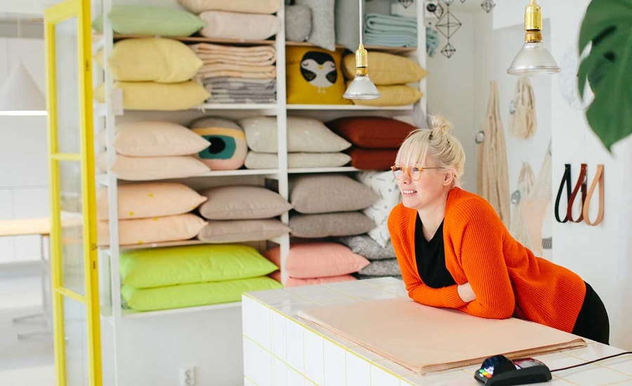 Dame lener seg over disken i interiørbutikken sin med betalingsterminal rett ved