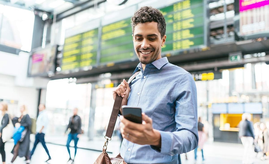 Mann på flyplass ser på mobiltelefonen, illustrasjon til mobilbank bedrift
