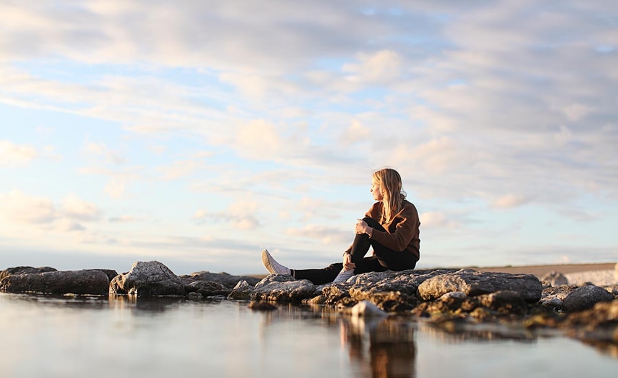 Ung jente sitter på fjærsteinene og ser utover havet, illustrasjon for grønn bank