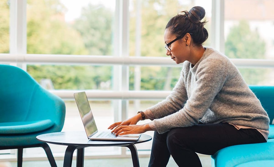 Dame sitter på en blå sofa og jobber på en laptop, til illustrasjon for kredittpolicy