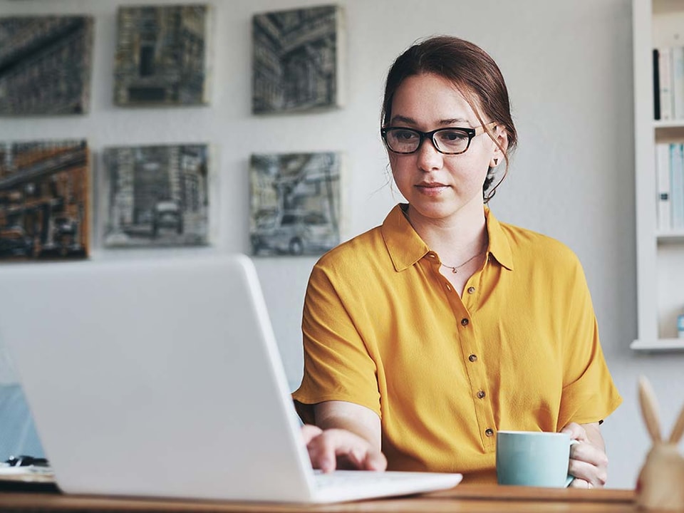 Dame med kaffekopp sitter og jobber på en PC, til illustrasjon for eFaktura