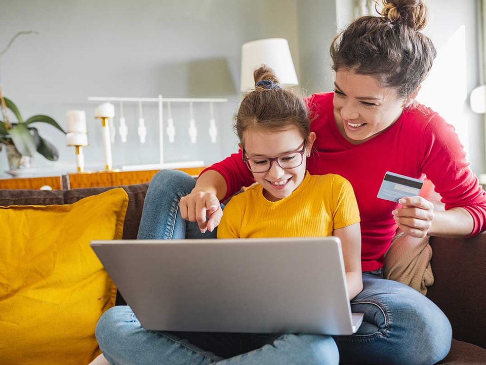 Mor og barn ser på pc med bankkort i handa, til illustrasjon og barn og penger