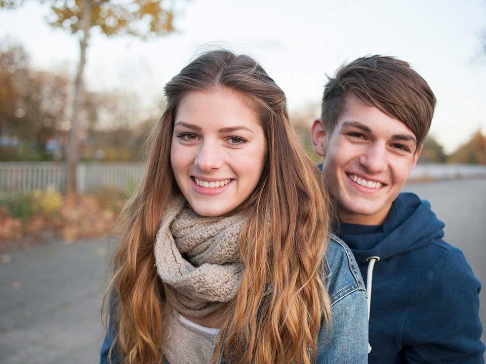 Ung jente og gutt smiler, med løv i bakgrunnen, til illustrasjon for endelig myndig