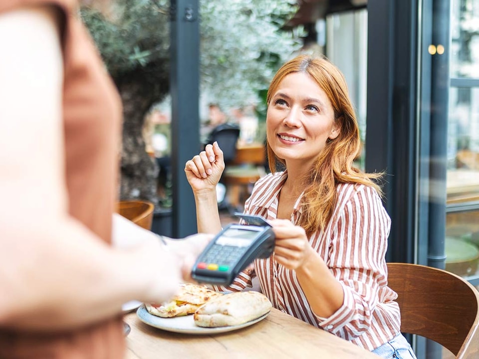 Dame på cafe tapper kort på terminal, til illustrasjon for bankkort