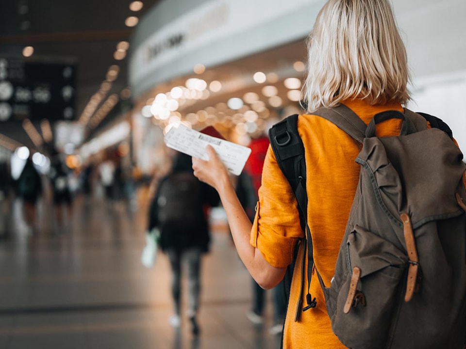 Dame med sekk og holder en flybillett i hånda på en flyplass, til illustrasjon for kredittkort