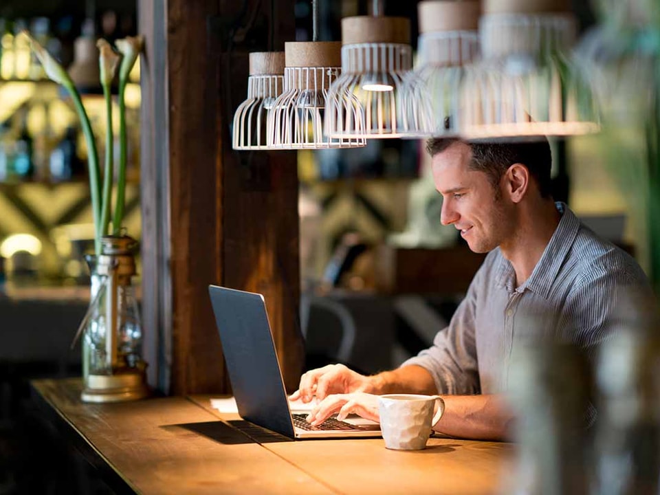 Mann sitter på cafe og ser på laptop, til illustrasjon for mobil-og nettbank