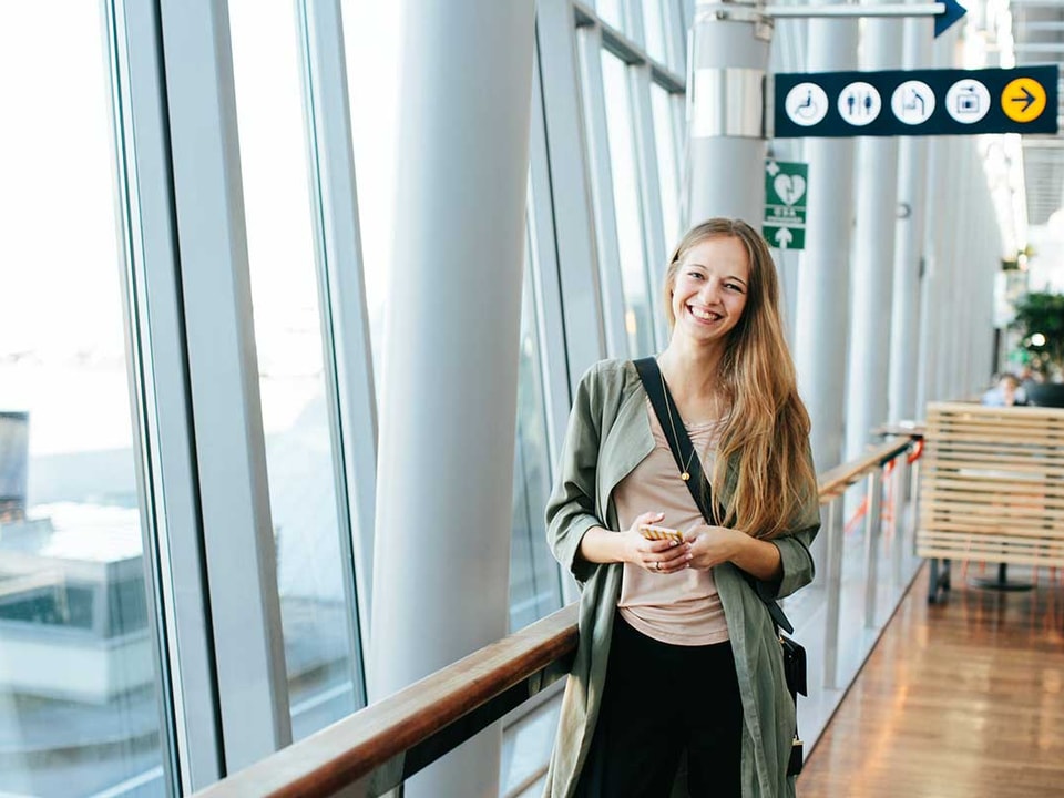 Jente står på flyplassen med mobilen i hånda, til illustrasjon for mobilbank