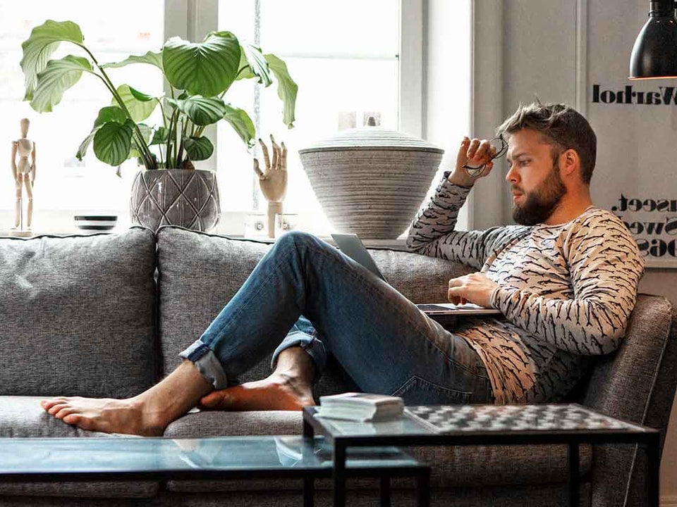 Mann sitter på sofaen og ser på laptop, til illustrasjon for nettbank