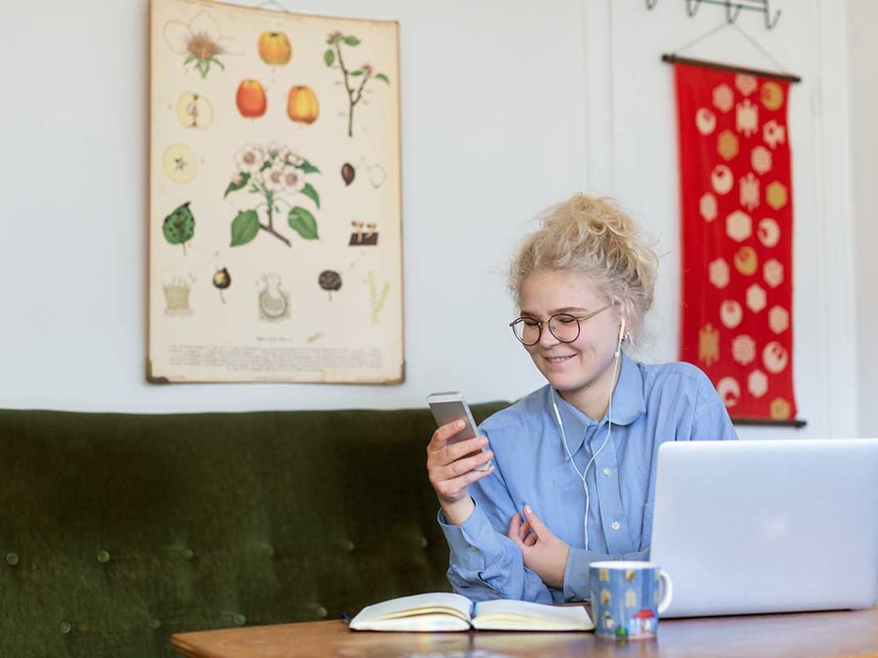 Jente sitter i grønn sofa og ser på mobilen med hodetelefoner, til illustrasjon for husleiekontrakt