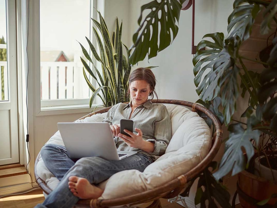Dame slapper av i stolen med mobil og pc, til illustrasjon for økt boliglånsrente