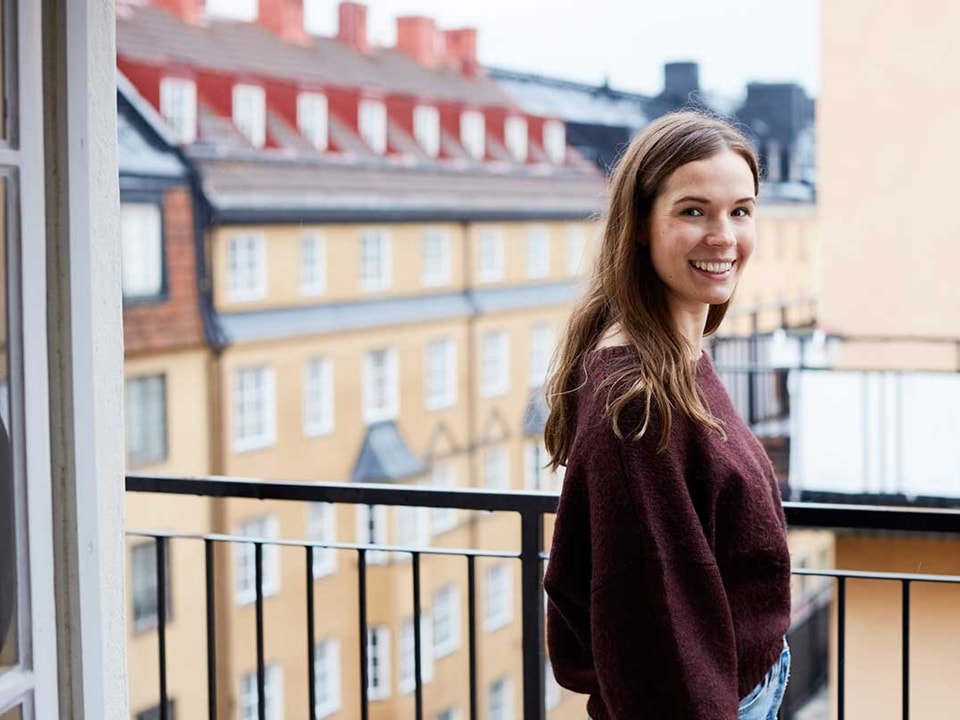 Ung jente står på en balkong og smiler, til illustrasjon for førstegangskjøp av bolig