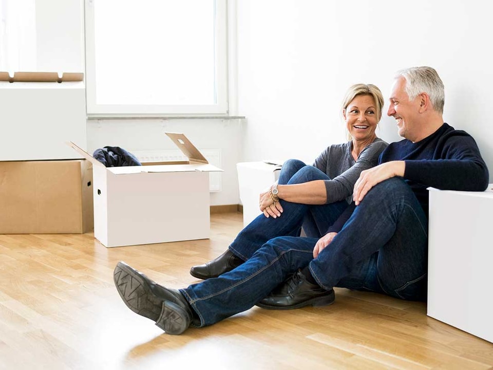 Par sitter på gulvet med flytteesker, til illustrasjon for å selge bolig