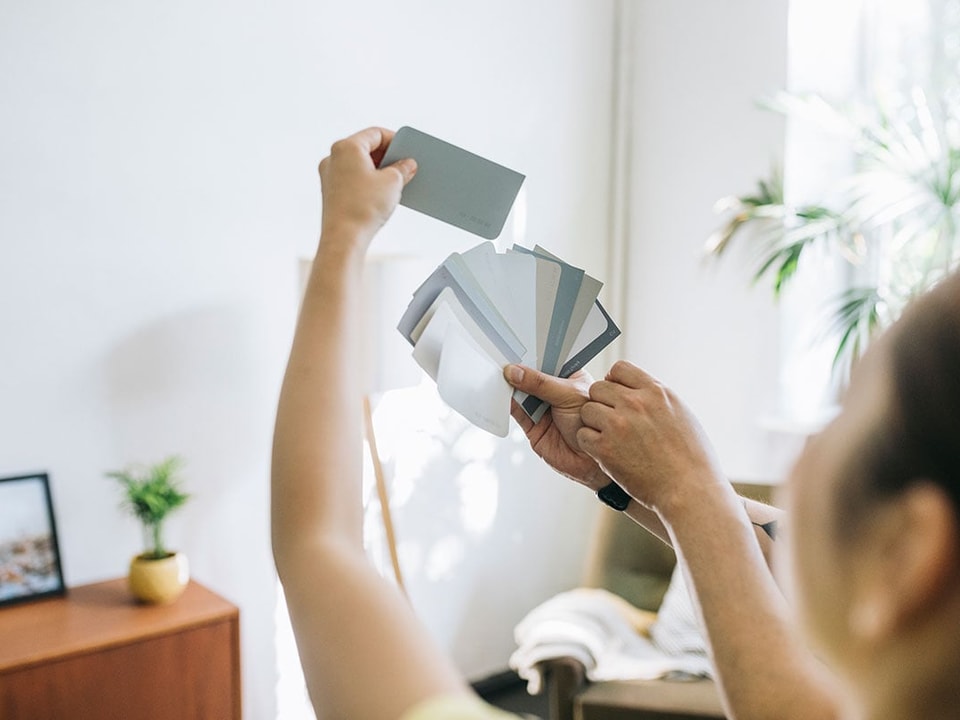 Dame ser på fargerpøver mot vegg, til illustrasjon for tips til oppussing