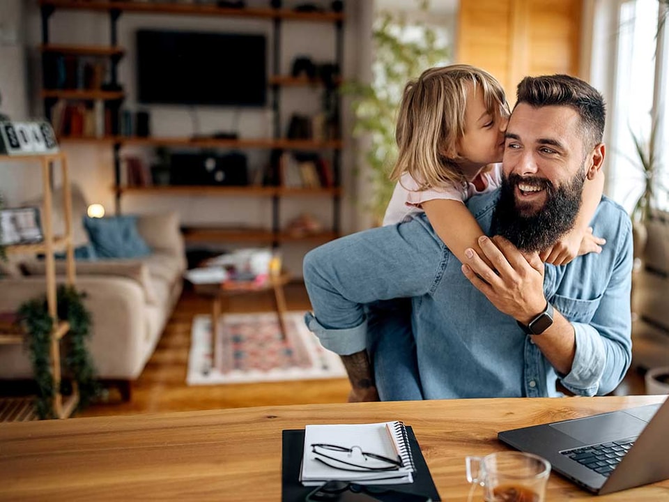 Mann sitter og jobber med et barn som klatrer på ryggen, til illustrasjon for fastrentelån