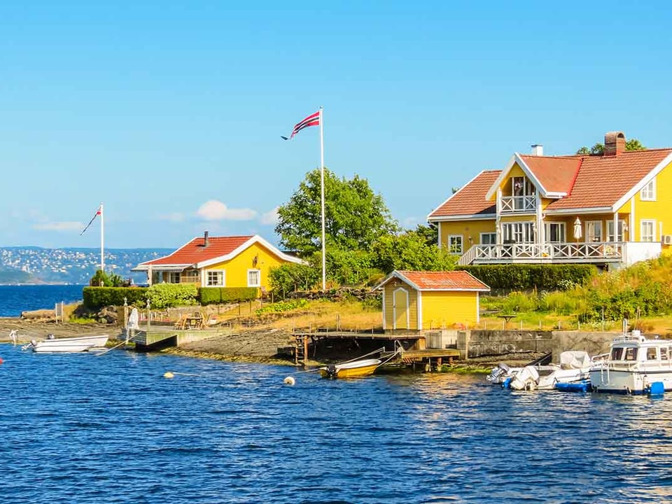Fritidsbolig ved sjøen i Norge med båter og båthus, til illustrasjon for kjøpe hytte