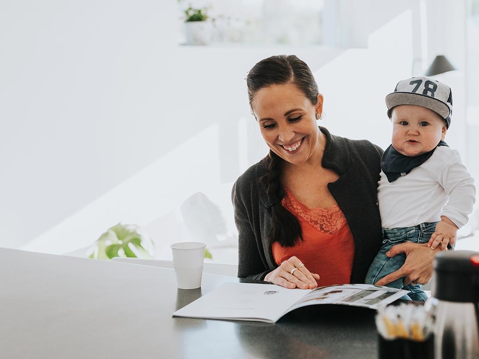 Kvinne holder et barn og ser på prospekter for å kjøpe ny bolig