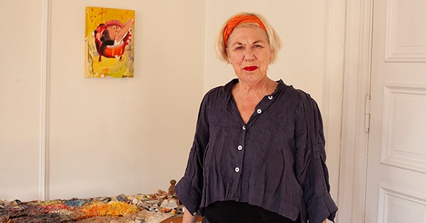 Bente er SeniorLånskunde i BN Bank og står i sitt eget hjem med fargerikt bilde bak, til illustrasjon for SeniorLån