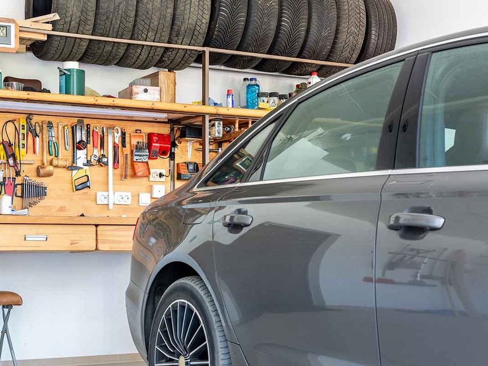 Bil er rygget inn i garasje som har lagringsplass for dekk og oppbevaring for verktøy, til illustrasjon for bygge garasje