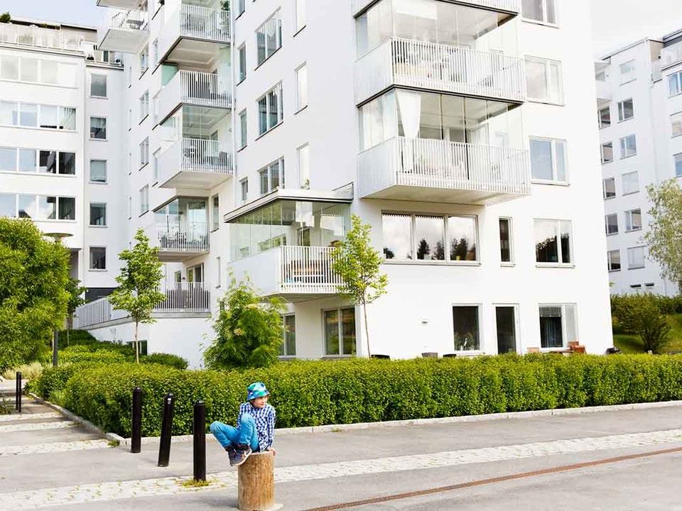 Gutt med bøttehatt sitter på en stokk fremfor en boligblokk, til illustrasjon for sekundærbolig