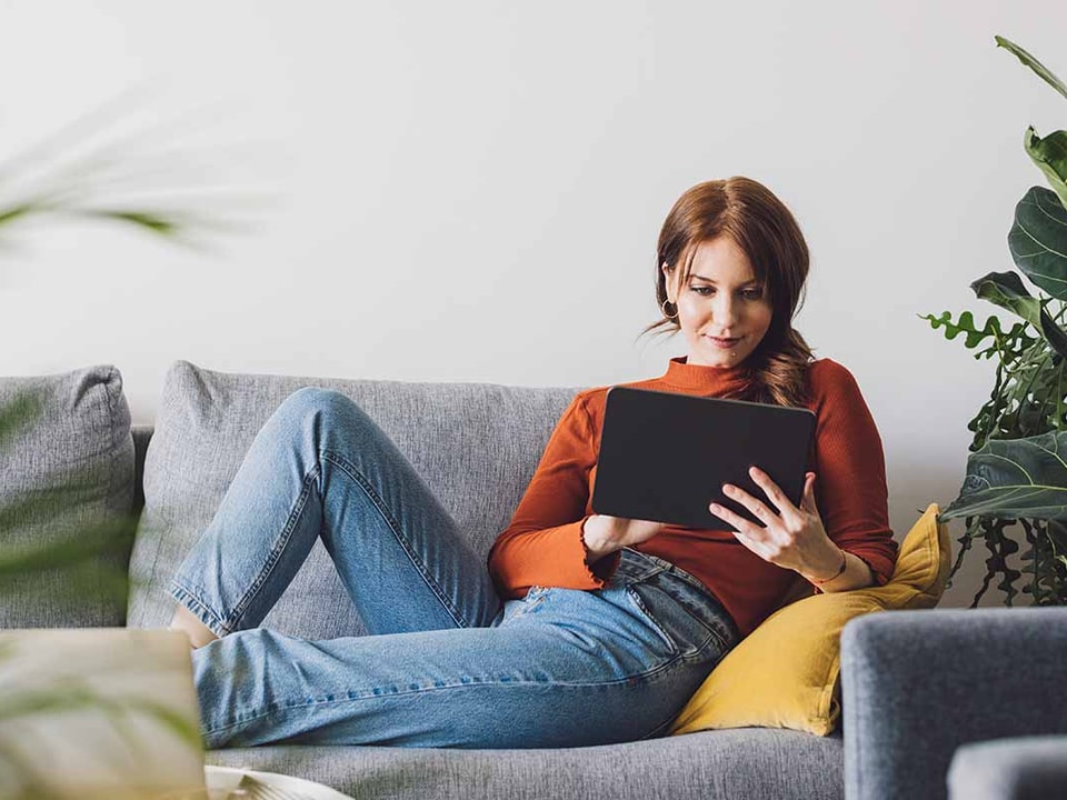 Dame sitter i sofa og leser på nettbrett, til illustrasjon for logg inn i bn bank