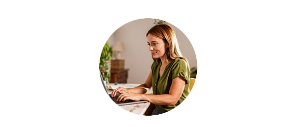 Kvinne med grønn bluse sitter og skriver på en laptop, til illustrasjon for spare til pensjon